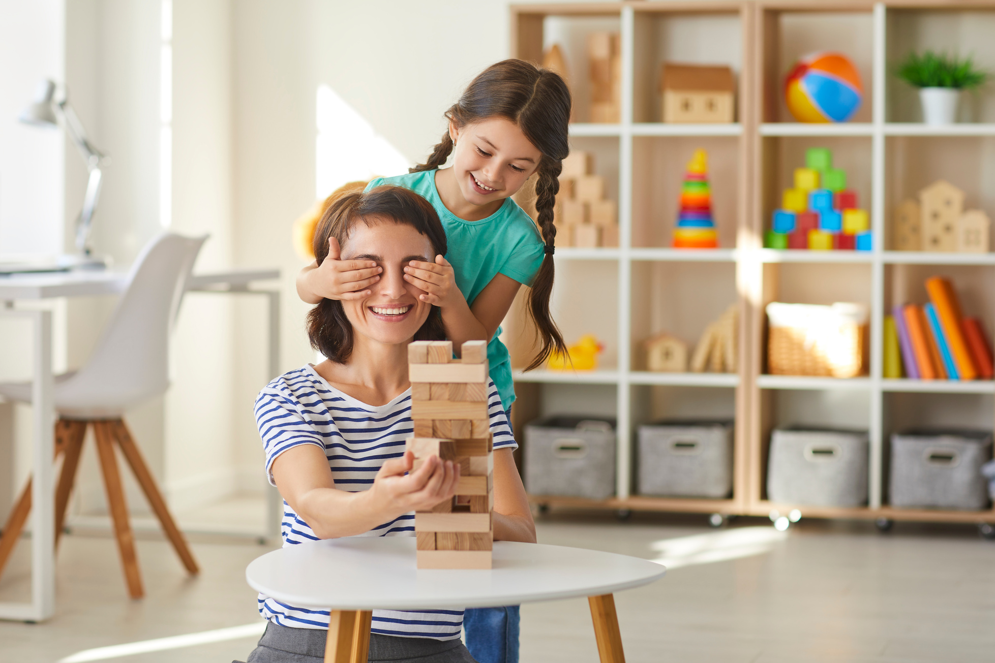 Little Daughter Putting Hands over Mommy's Eyes While Playing with Wood Blocks in Modern Nursery